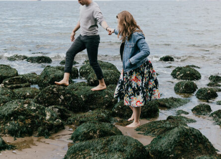 couple with contracting out agreement holding hands while walking over beach rocks